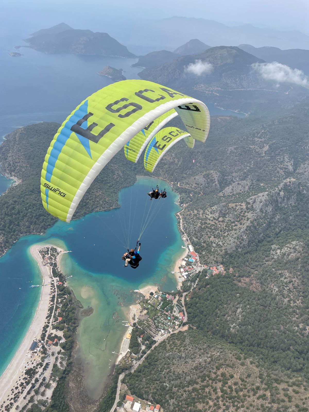A tandem paraglider in flight high above Ölüdeniz, with the Blue Lagoon, Belcekız beach and the coastline far below