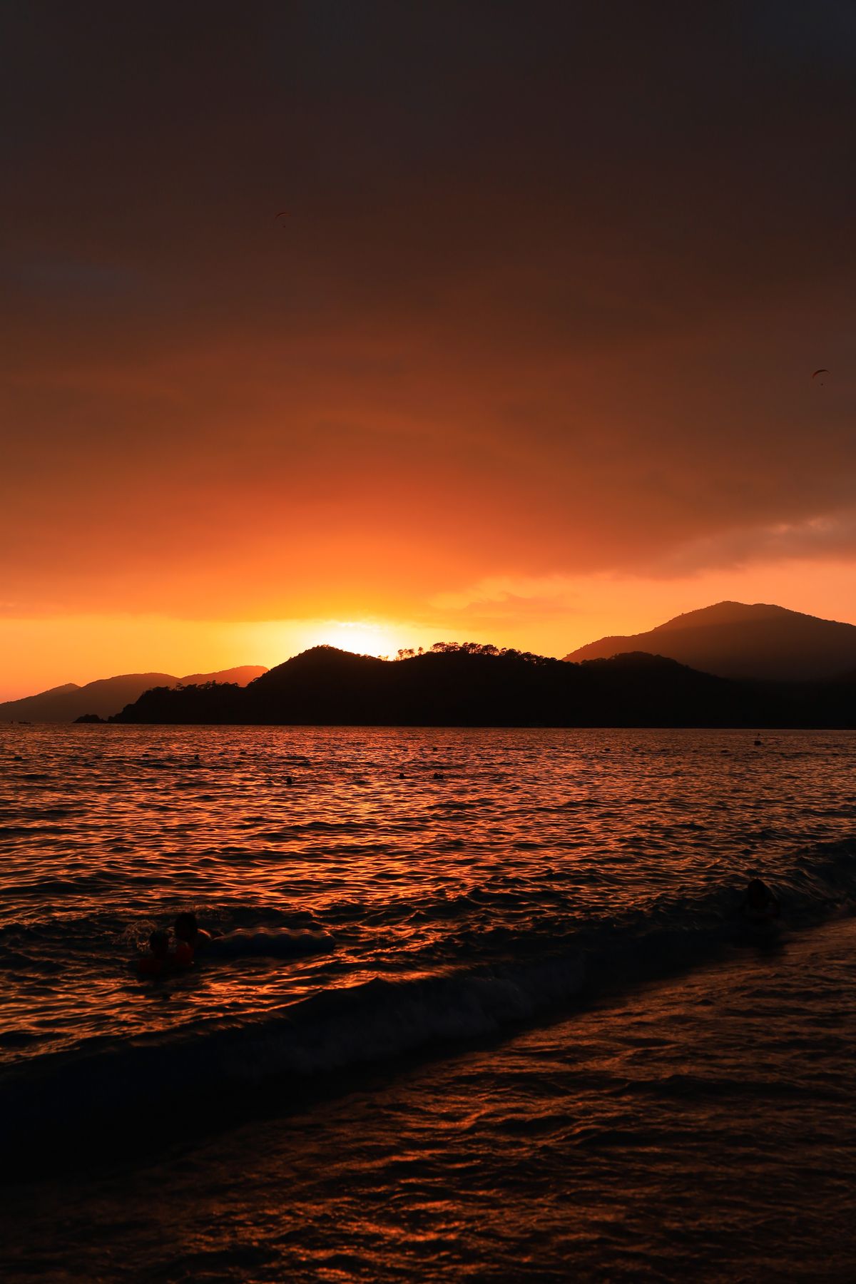 Sun setting behind a wooded headland across the bay, water burnt orange