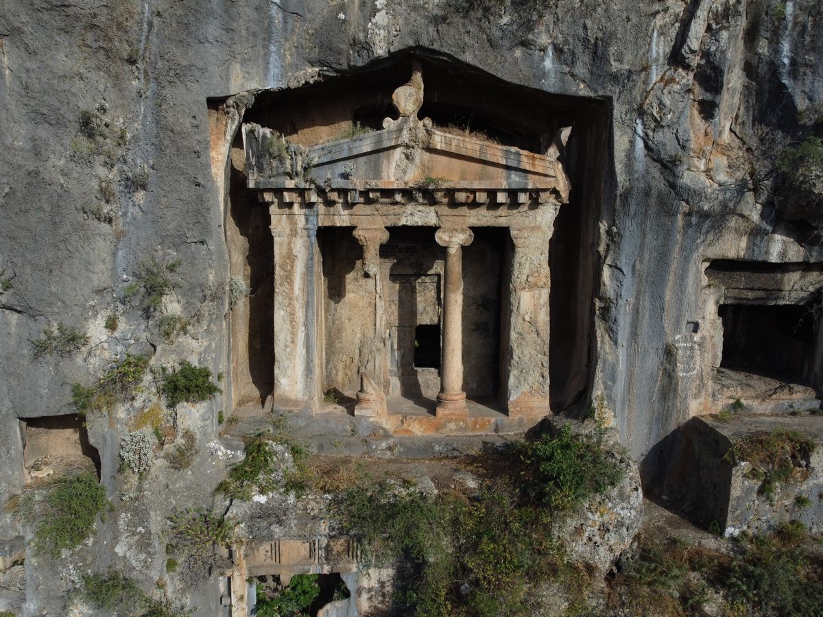 Lycian rock-cut tomb carved into a cliff face with a temple facade, two columns and a pediment above a dark doorway